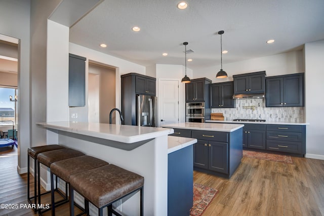 kitchen with decorative light fixtures, a kitchen bar, decorative backsplash, kitchen peninsula, and stainless steel appliances