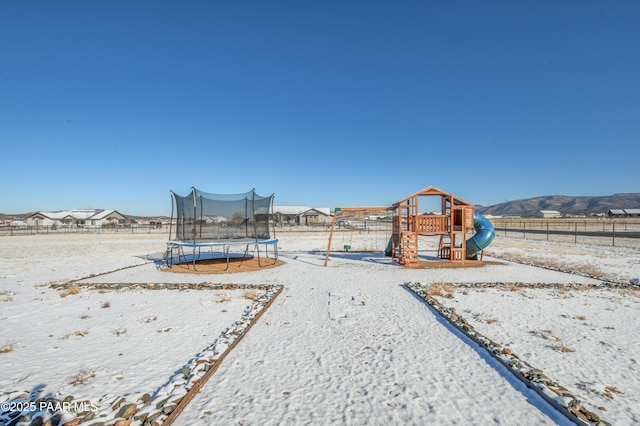 yard covered in snow featuring a trampoline, a mountain view, and a playground