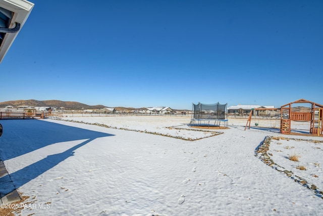 yard covered in snow featuring a mountain view, a trampoline, and a playground