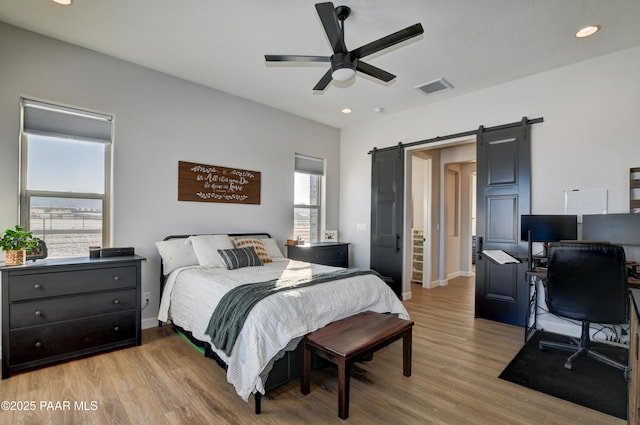 bedroom featuring ceiling fan, a barn door, and light hardwood / wood-style flooring