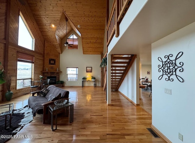 living area featuring light wood finished floors, visible vents, a glass covered fireplace, wood ceiling, and stairs