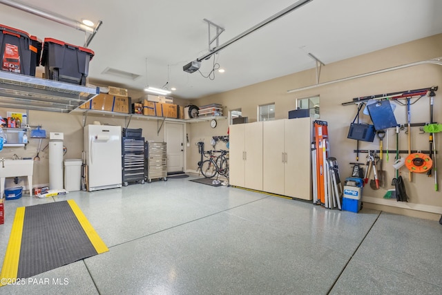 garage featuring sink, white fridge, and a garage door opener