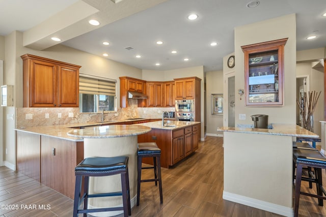 kitchen featuring a kitchen bar, kitchen peninsula, black electric cooktop, light stone countertops, and a kitchen island