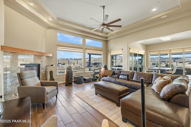 living room with a tile fireplace, ceiling fan, and a tray ceiling