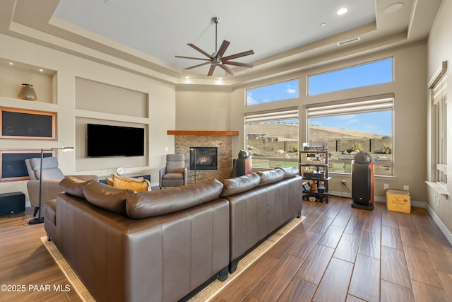 living room with built in shelves, a fireplace, ceiling fan, and a tray ceiling