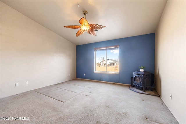 carpeted empty room with ceiling fan, vaulted ceiling, and a wood stove