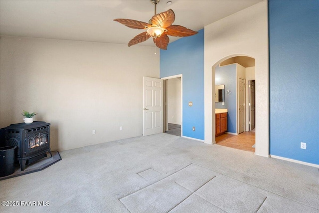 unfurnished bedroom with a high ceiling, ensuite bath, a wood stove, ceiling fan, and light colored carpet