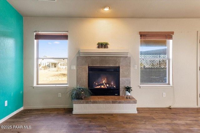 living room featuring wood-type flooring, a healthy amount of sunlight, and a tiled fireplace