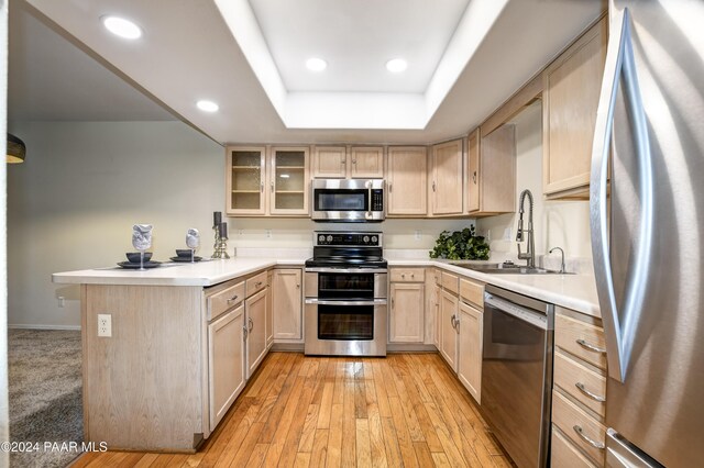 kitchen with sink, light brown cabinetry, light hardwood / wood-style floors, kitchen peninsula, and stainless steel appliances