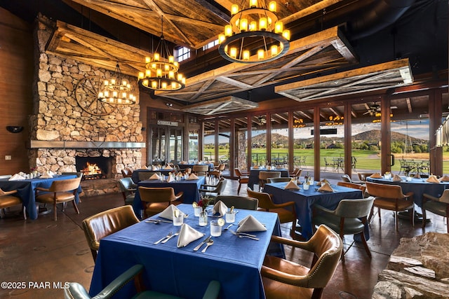 dining area with ceiling fan with notable chandelier and a stone fireplace