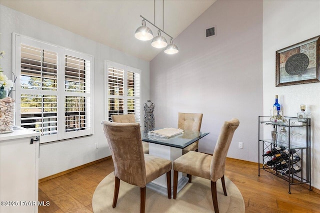 dining space with visible vents, vaulted ceiling, baseboards, and wood finished floors