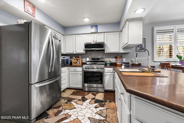 kitchen with dark countertops, white cabinetry, stainless steel appliances, and a sink