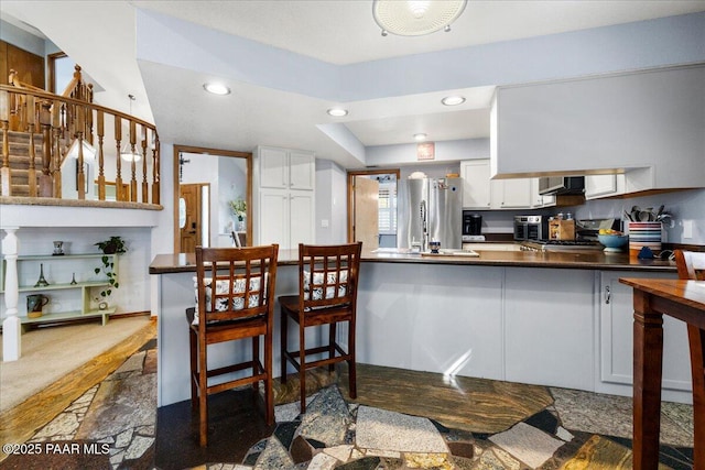 kitchen with a peninsula, stove, white cabinetry, freestanding refrigerator, and dark countertops