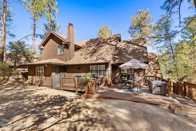 rear view of property with a shingled roof, a chimney, and a wooden deck