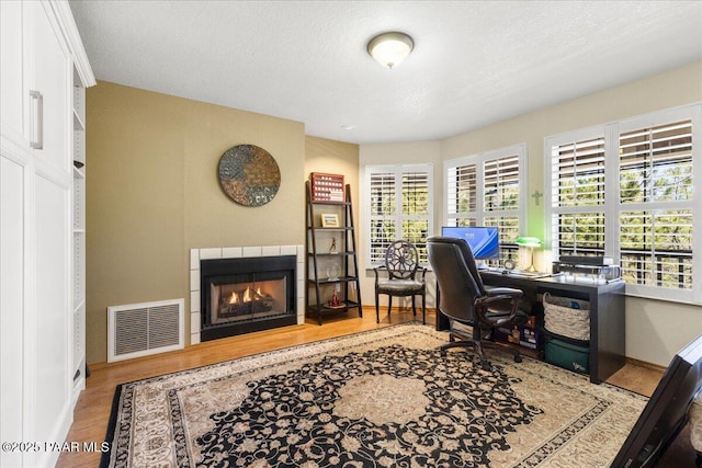 home office with a fireplace, visible vents, a textured ceiling, wood finished floors, and baseboards