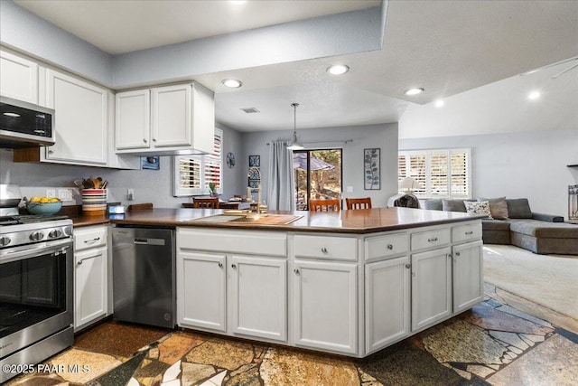 kitchen with stainless steel appliances, a peninsula, white cabinetry, open floor plan, and dark countertops