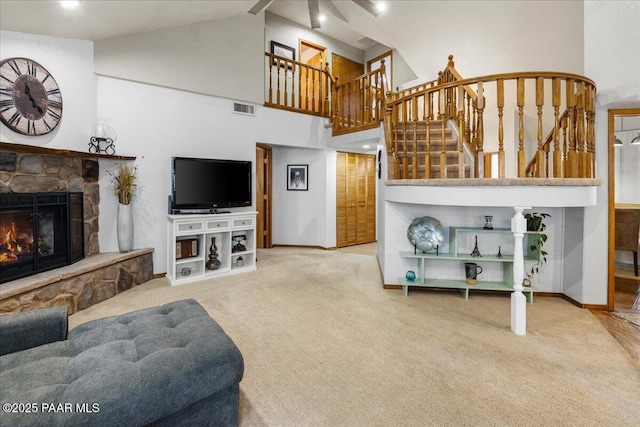 living area with carpet floors, stairway, visible vents, and a stone fireplace