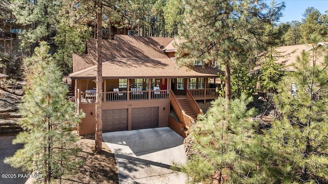 rustic home with a garage, concrete driveway, roof with shingles, stairs, and a porch