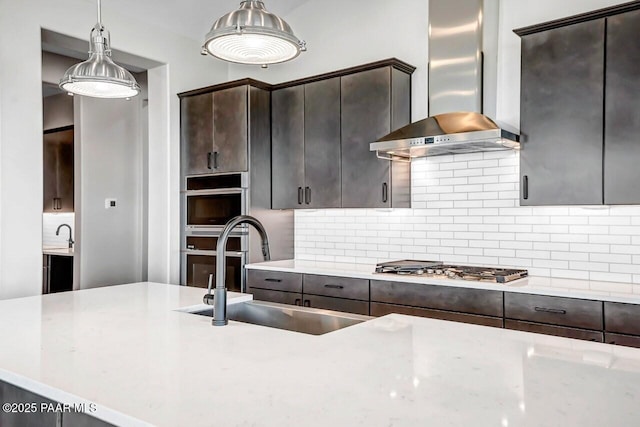 kitchen with pendant lighting, sink, dark brown cabinets, light stone countertops, and wall chimney exhaust hood