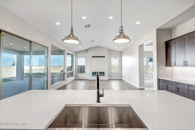 kitchen with lofted ceiling, sink, decorative backsplash, light stone counters, and dark brown cabinetry