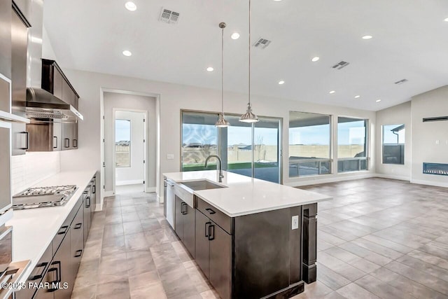 kitchen with appliances with stainless steel finishes, pendant lighting, sink, a center island with sink, and wall chimney exhaust hood