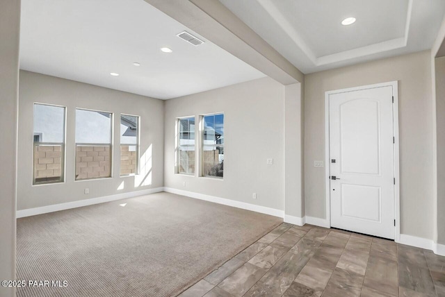 foyer entrance with a raised ceiling and light carpet