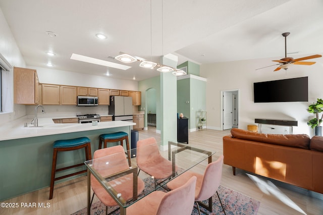 dining room with light wood-type flooring, ceiling fan, sink, and vaulted ceiling with skylight