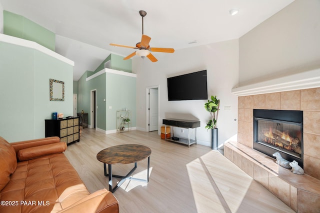 living room featuring light wood-type flooring, a tiled fireplace, high vaulted ceiling, and ceiling fan