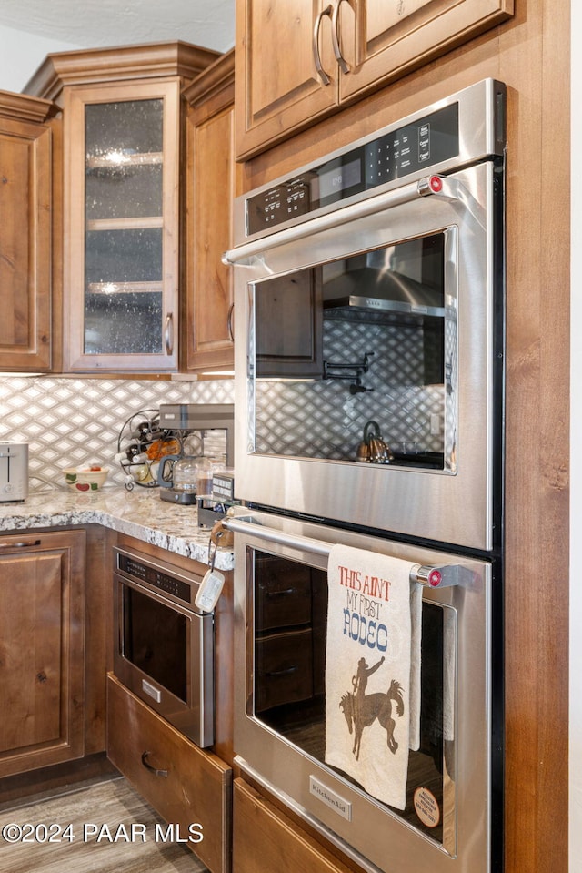 kitchen featuring double oven, backsplash, light stone countertops, and light hardwood / wood-style flooring