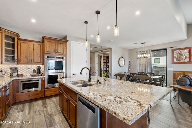 kitchen with appliances with stainless steel finishes, a kitchen island with sink, sink, decorative light fixtures, and hardwood / wood-style flooring