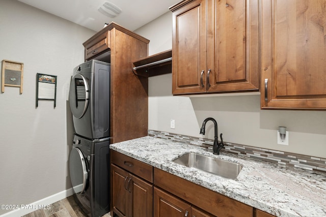 kitchen with light stone countertops, sink, stacked washer and clothes dryer, and hardwood / wood-style flooring