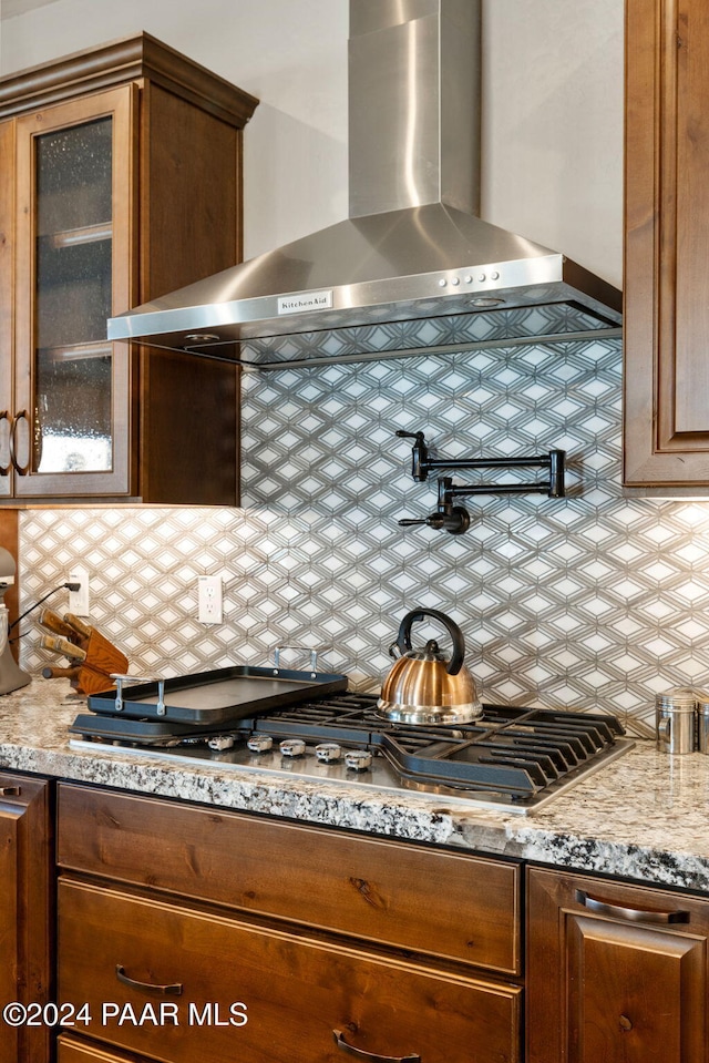 kitchen with backsplash, light stone counters, wall chimney exhaust hood, and stainless steel gas cooktop