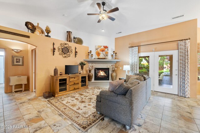 living room featuring a ceiling fan, a warm lit fireplace, and arched walkways