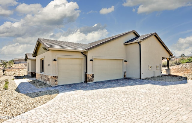 view of home's exterior with driveway, stone siding, a tiled roof, a garage, and stucco siding