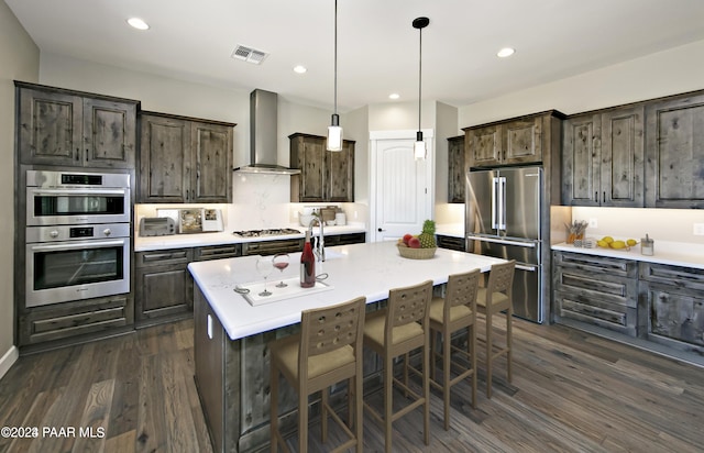 kitchen featuring wall chimney range hood, dark brown cabinets, stainless steel appliances, visible vents, and dark wood-style floors
