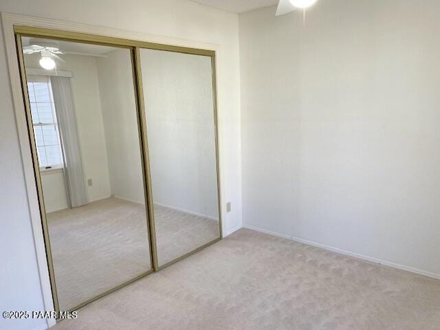 unfurnished bedroom featuring light carpet, a closet, and ceiling fan