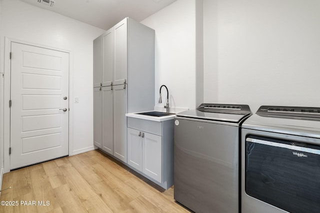 clothes washing area featuring light wood finished floors, cabinet space, visible vents, washing machine and dryer, and a sink