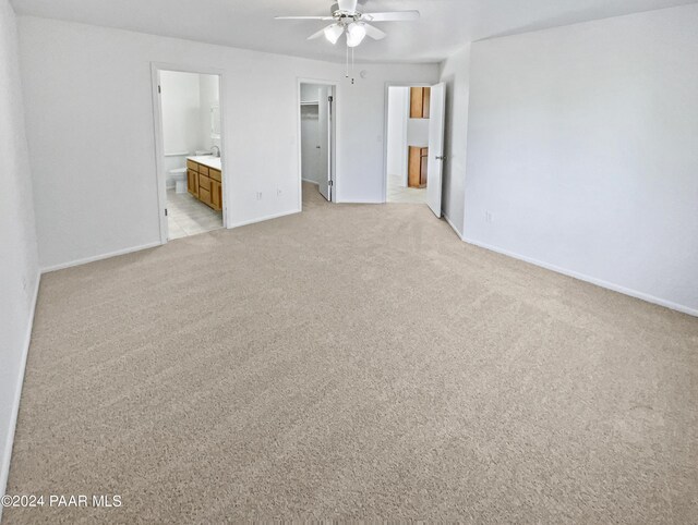 unfurnished bedroom featuring light colored carpet, ensuite bath, and ceiling fan