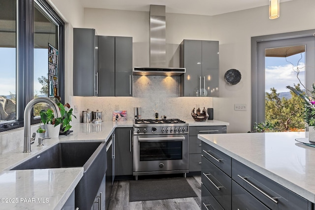 kitchen featuring sink, stainless steel appliances, wall chimney range hood, gray cabinets, and decorative backsplash