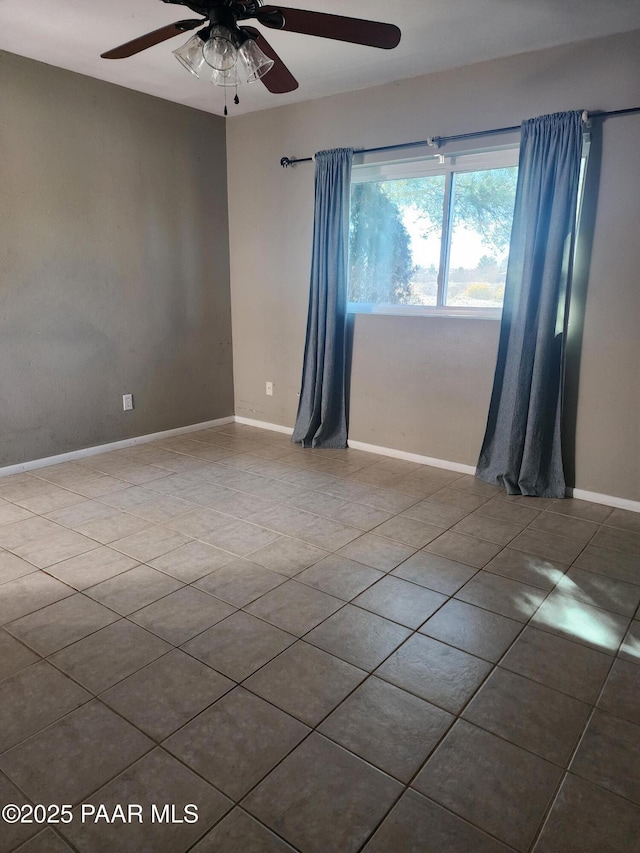 tiled empty room featuring a ceiling fan and baseboards