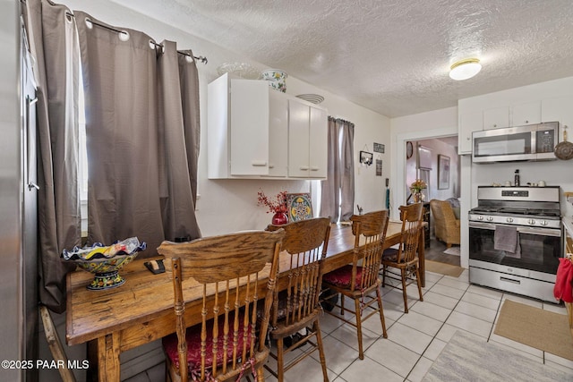 kitchen with light tile patterned floors, appliances with stainless steel finishes, white cabinetry, and a textured ceiling