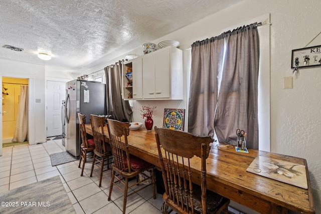 dining area with light tile patterned floors, visible vents, a textured ceiling, and a textured wall