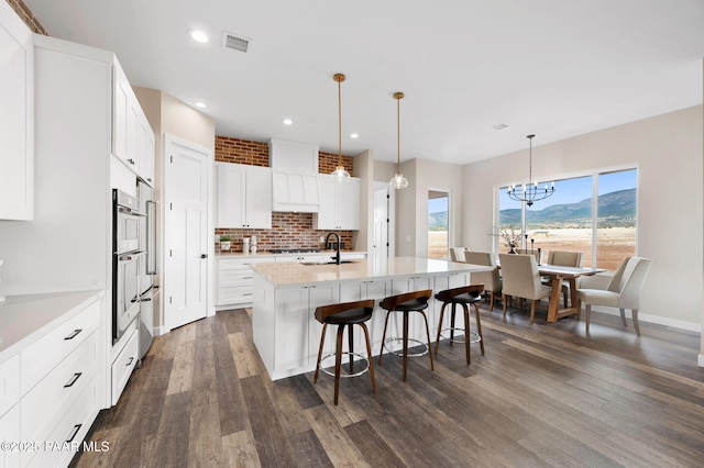 kitchen with light countertops, a kitchen bar, dark wood-style floors, visible vents, and decorative backsplash