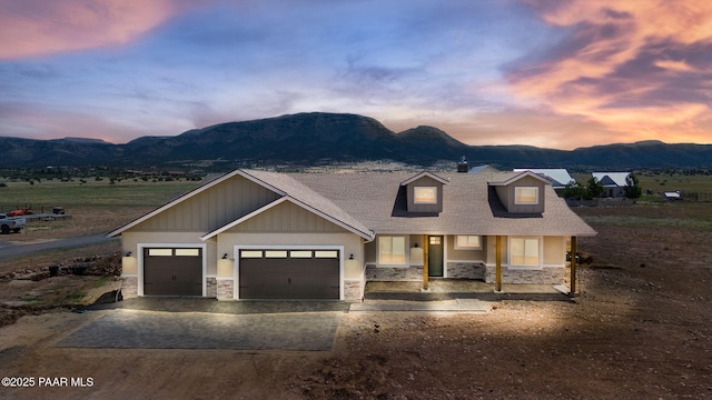 view of front of house featuring driveway, an attached garage, stone siding, and a mountain view