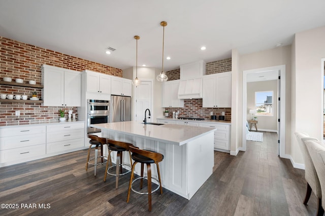 kitchen with a kitchen breakfast bar, a sink, a kitchen island with sink, appliances with stainless steel finishes, and custom exhaust hood