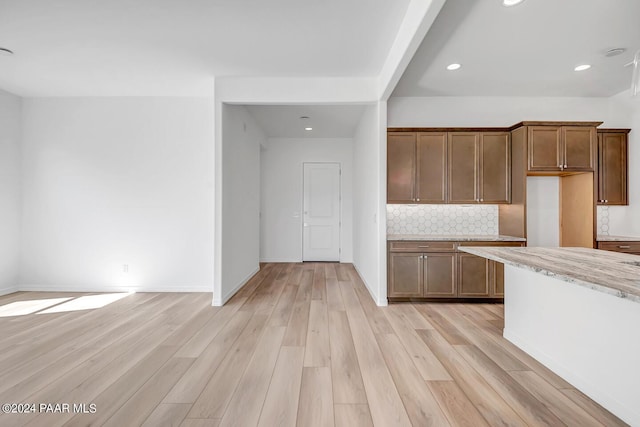 kitchen with tasteful backsplash, light wood-type flooring, and light stone counters