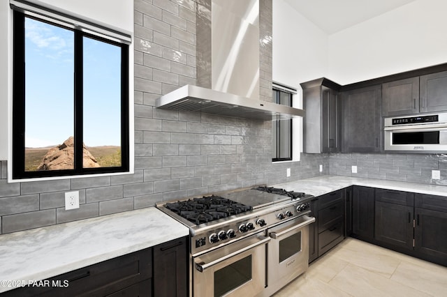 kitchen with backsplash, light tile patterned flooring, light stone countertops, appliances with stainless steel finishes, and wall chimney exhaust hood