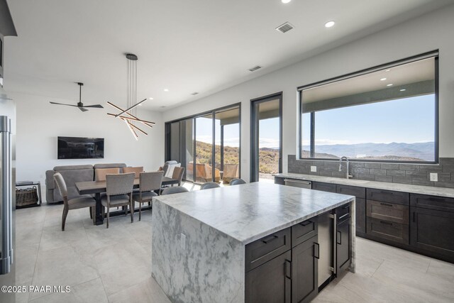 kitchen with ceiling fan with notable chandelier, a kitchen island, tasteful backsplash, sink, and a mountain view