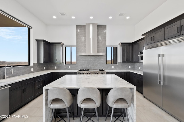 kitchen with tasteful backsplash, a kitchen island, sink, appliances with stainless steel finishes, and wall chimney exhaust hood