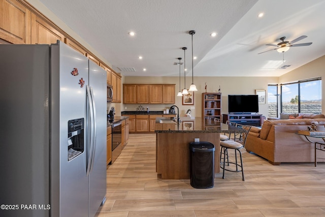 kitchen featuring appliances with stainless steel finishes, a breakfast bar, decorative light fixtures, an island with sink, and light wood-type flooring